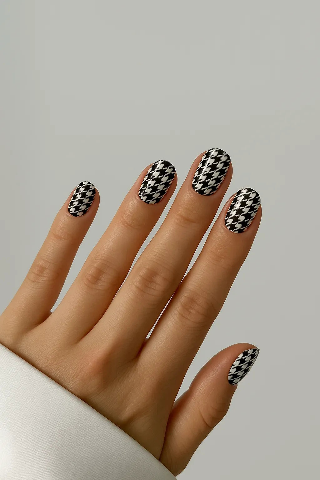 #type_manicure Hand with black and white houndstooth patterned nail wraps on a neutral background