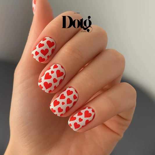 Hand with red and white heart-patterned nails against a neutral background