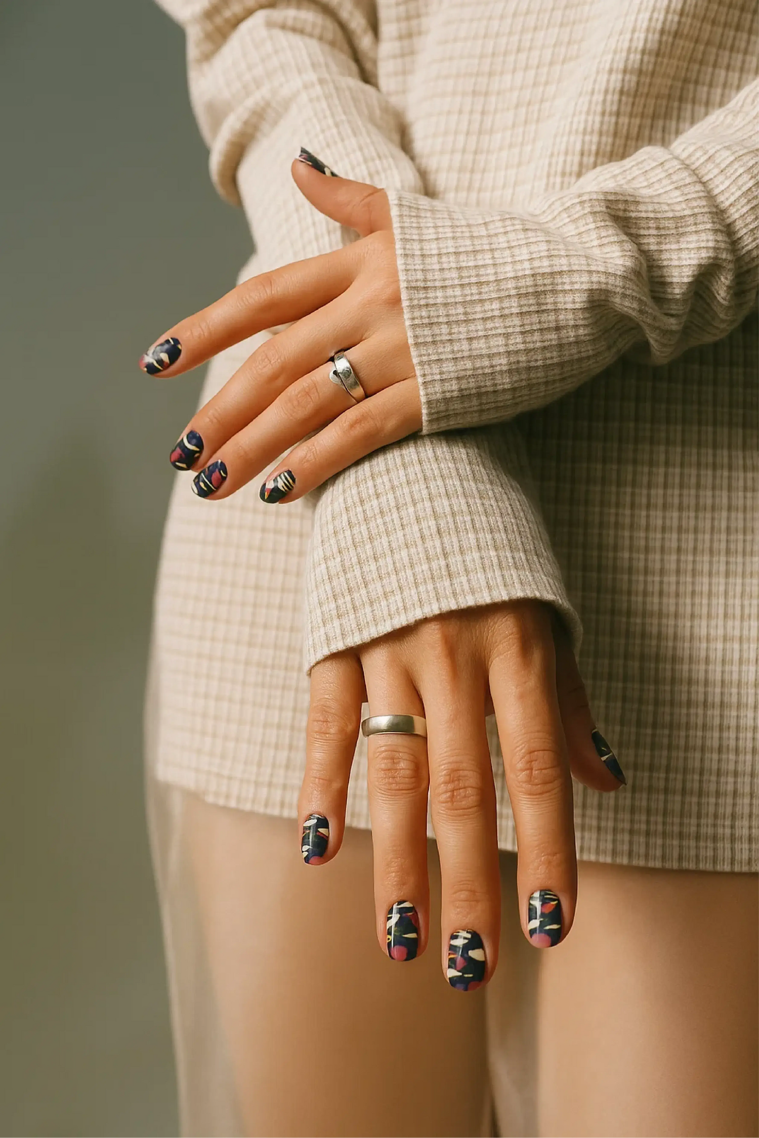 Close-up of hands with patterned nails wearing rings, against a neutral background