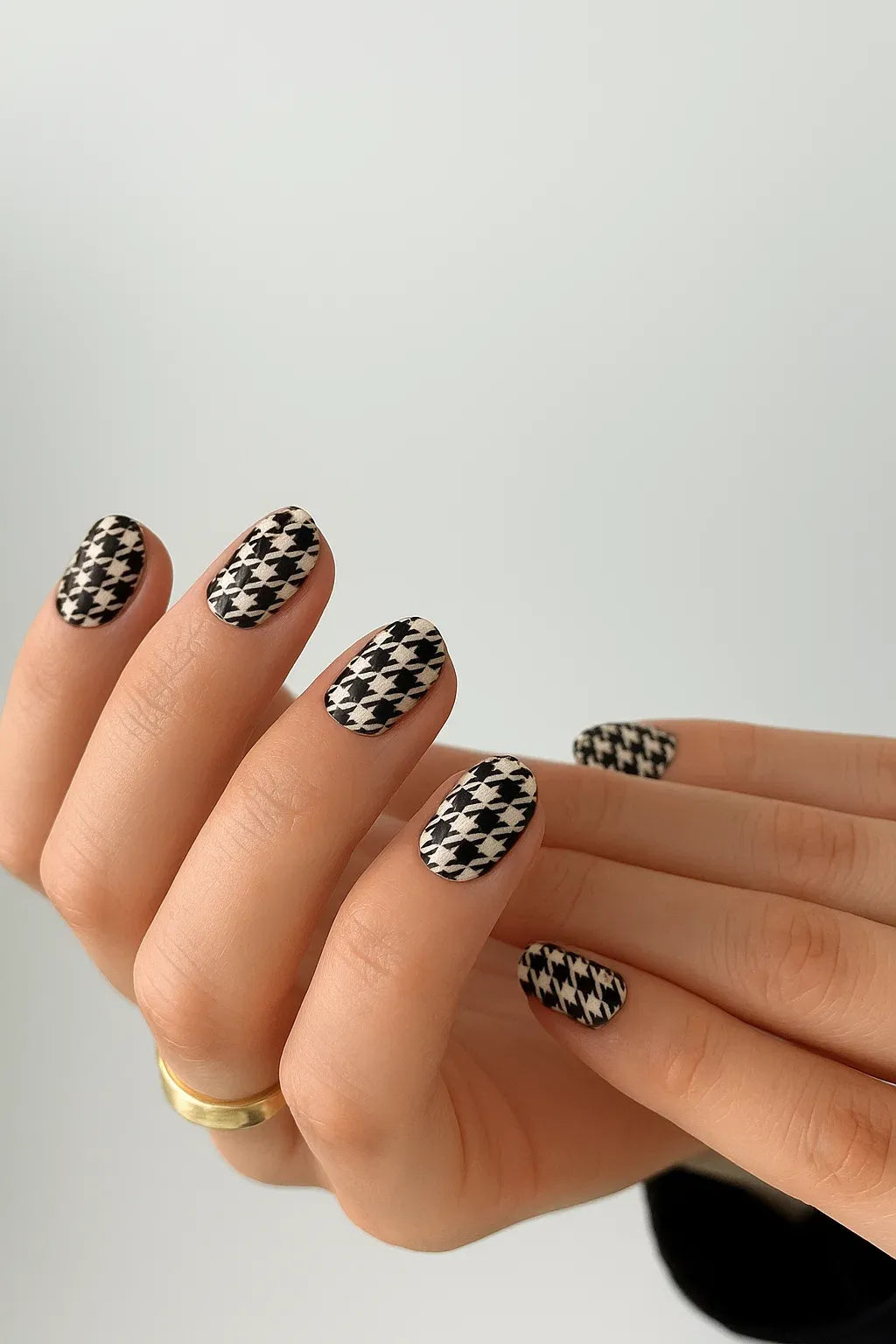 #type_manicure Hand with houndstooth patterned nail wraps nails on a plain background