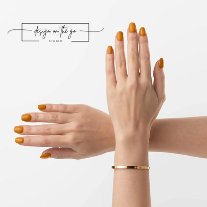 Two hands with orange nail polish and a gold bracelet on a light gray background.