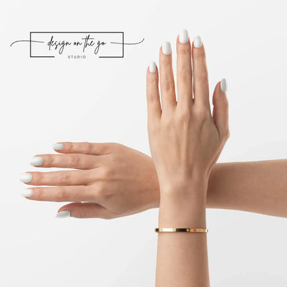 Gold bracelet on a hand with white nail polish against a light background
