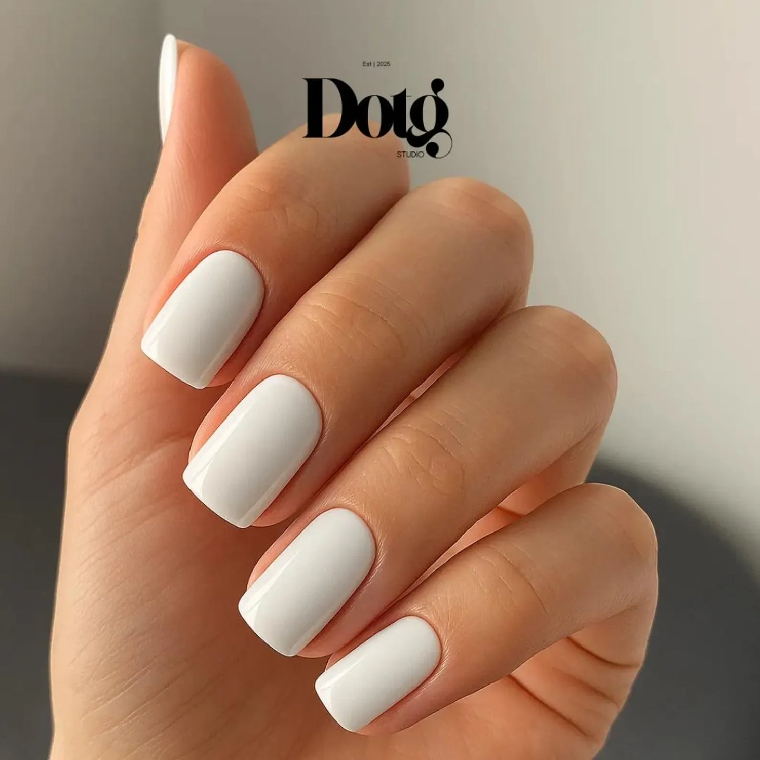 Hand with solid white nail wraps on a neutral background, featuring the Dotg Studio logo.