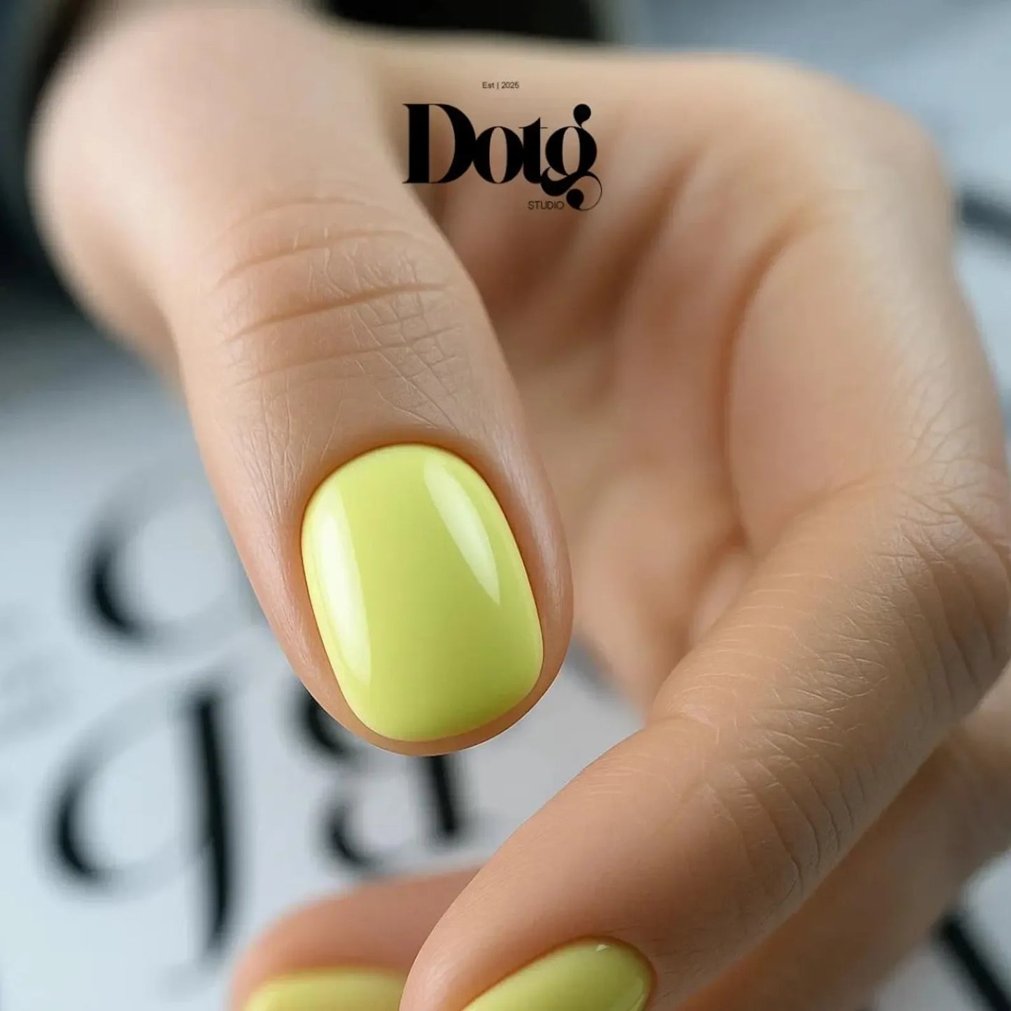 Close-up of a hand with a bright yellow nail, featuring the Dotg Studio logo.