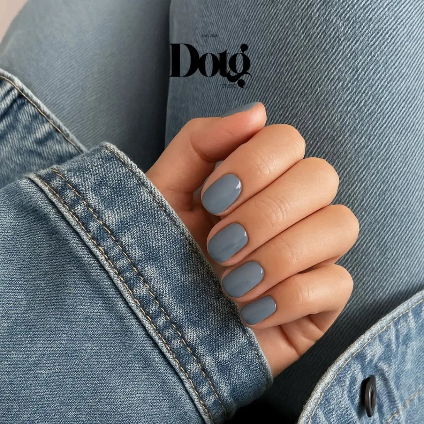 Hand with gray nail polish wearing a denim jacket, featuring the Dotg Studio logo.
