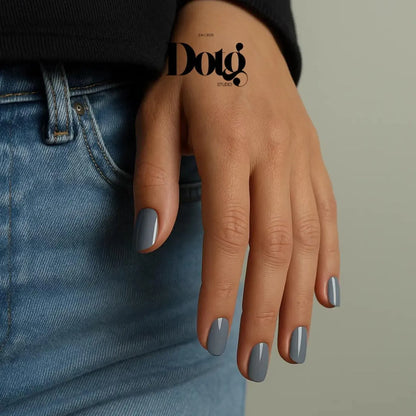 Hand with gray nail polish wearing a black sleeve and blue jeans on a neutral background