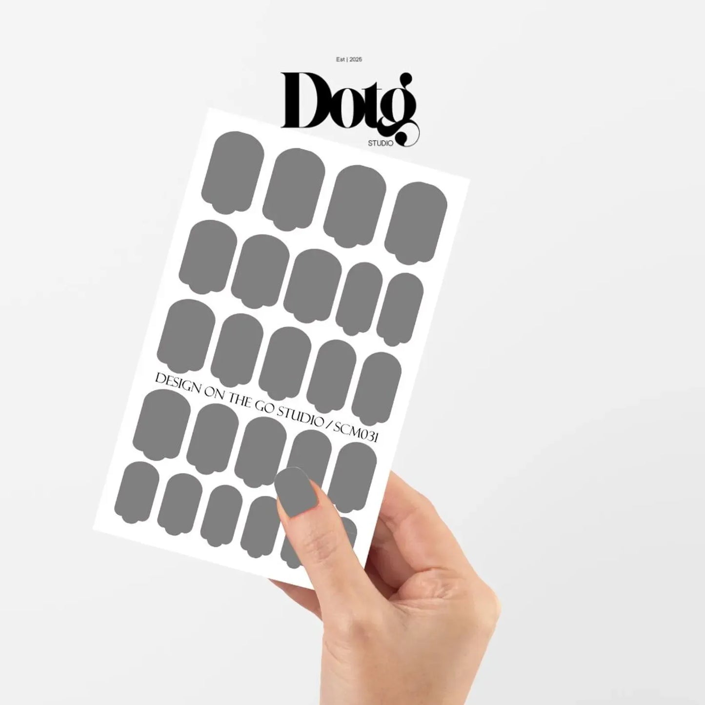 Sheet of gray nail stickers held by a hand with Doto Studios branding on a white background